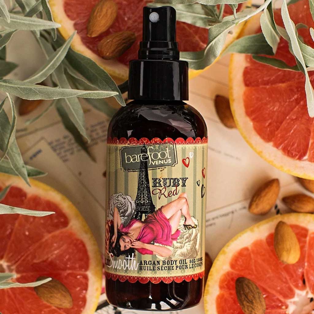 Barefoot Venus Ruby Red Argan body oil product with background of grapefruits, almonds and leaves.