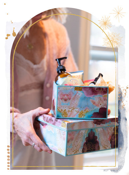 Person holding Barefoot Venus gift boxes with Barefoot Venus products surrounded by a decorative frame.
