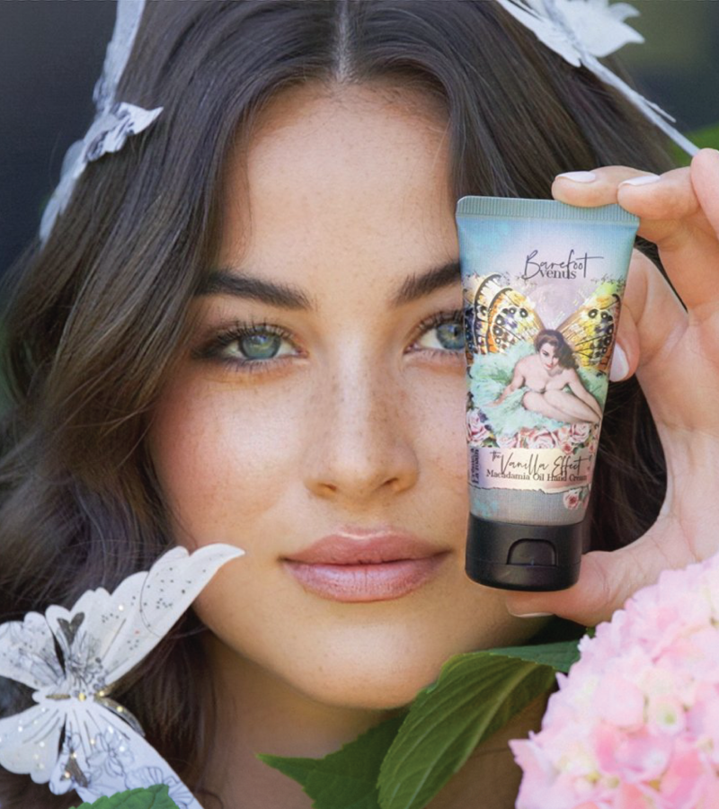 Woman holding a skincare product with a decorative label, surrounded by flowers and butterfly wings.